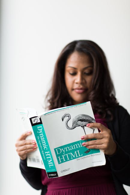 A woman with long dark hair and light brown skin is reading a book titled 'Dynamic HTML' by O'Reilly, holding it with both hands, with her right index finger resting on the cover illustration of a fla